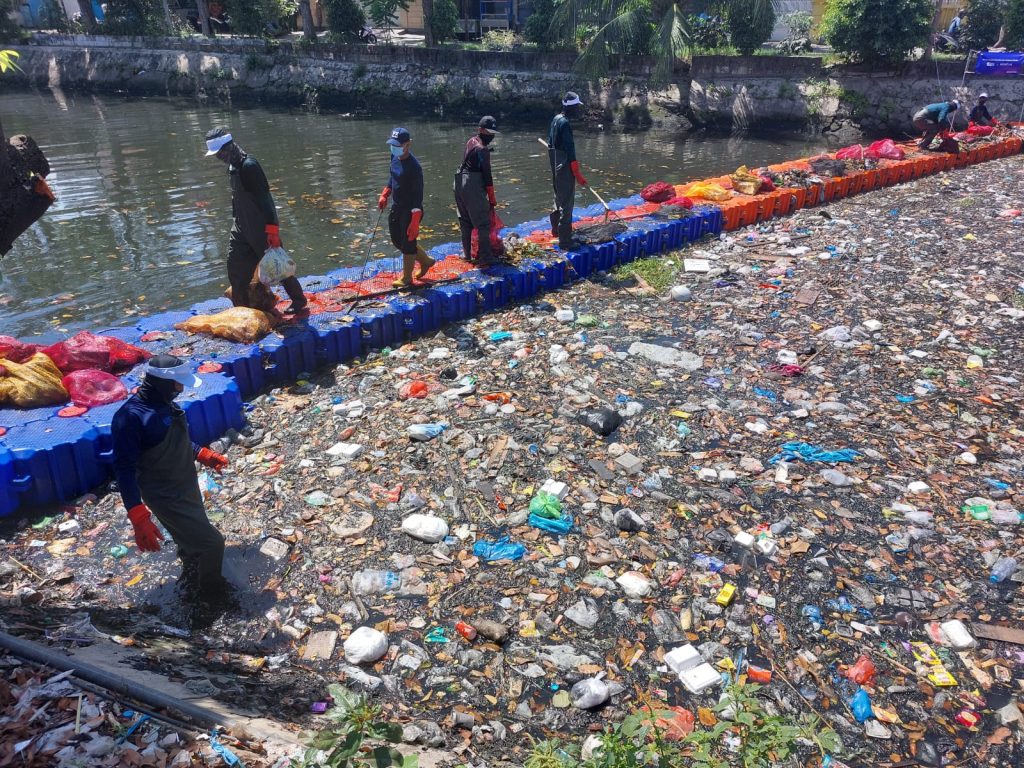 Volunteers carry bags of collected waste while cleaning Kali Tebu River.